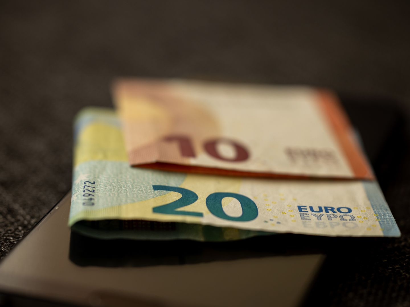 A detailed close up shot of 10 and 20 euro banknotes placed on a smartphone, representing finance and technology.