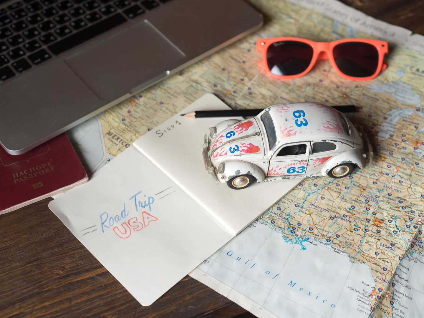 Flat lay of a road trip plan featuring maps, passport, toy car, and travel essentials.