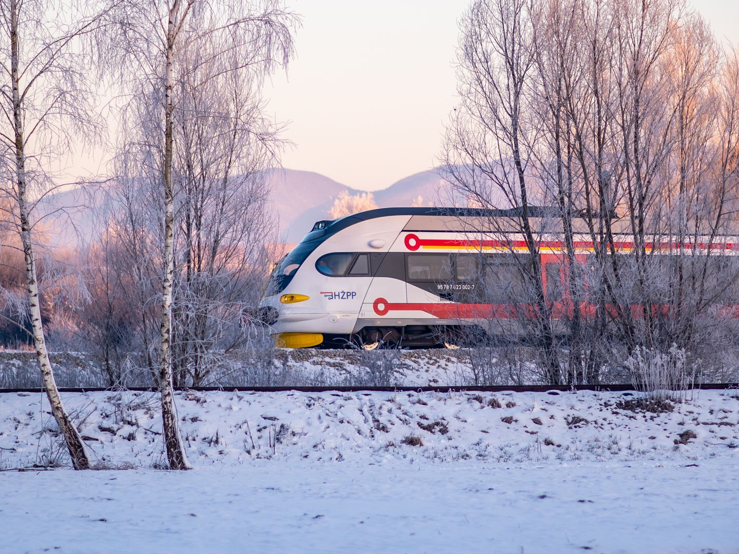 A sleek passenger train travels through a snowy landscape with frosty trees, epitomizing winter travel.