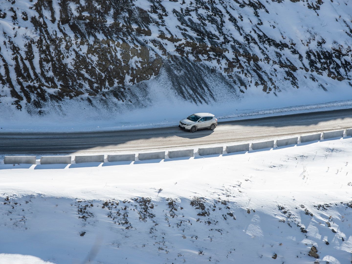 A vehicle driving along a snow covered mountain road, highlighting winter travel and scenic beauty.