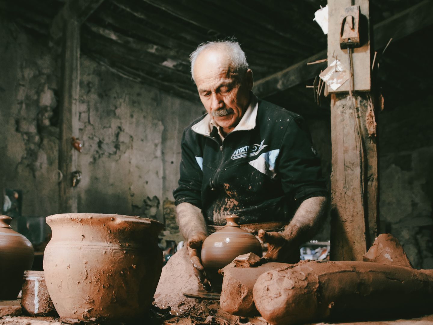 Senior man skillfully shaping clay pots in a rustic pottery workshop, showcasing traditional craftsmanship.